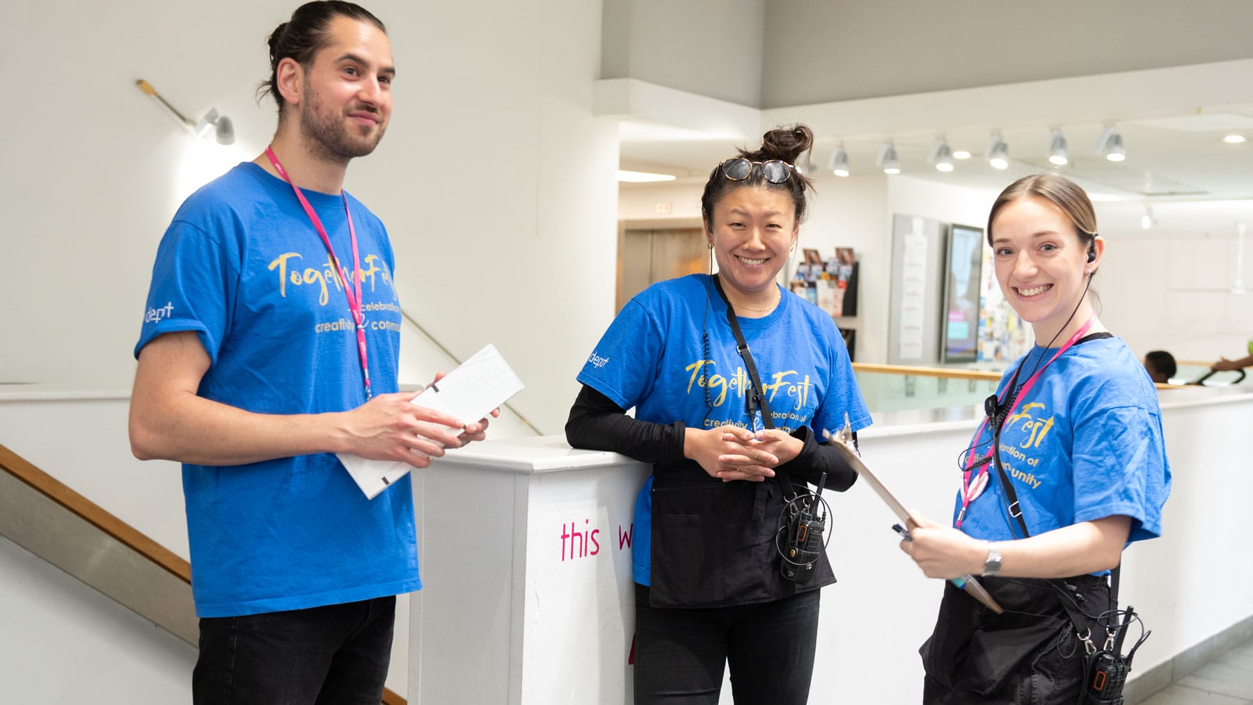 Three artsdepot staff members pictured at a family fun day, wearing blue tshirts and smiling at the camera
