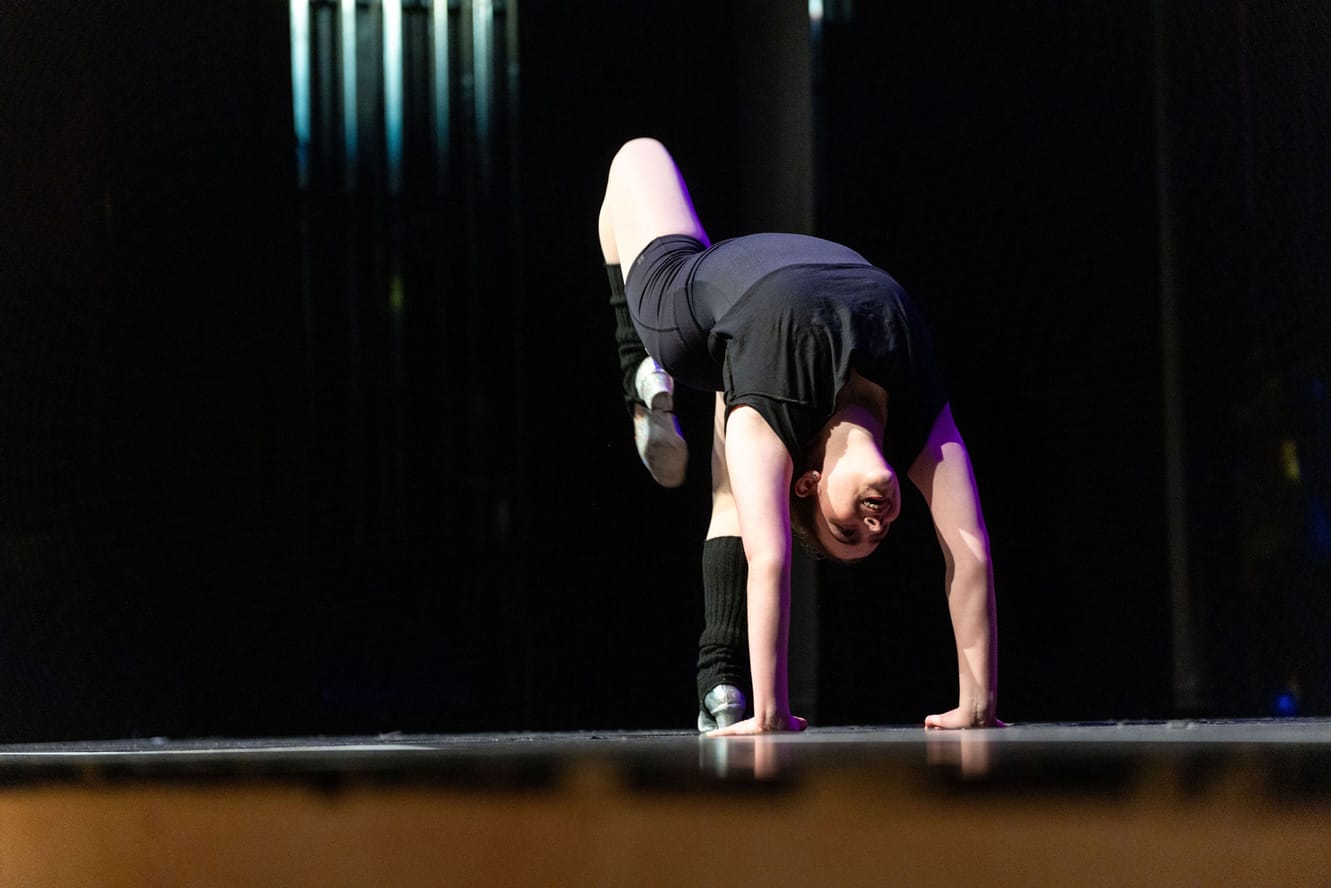 A young performer on stage performs a gymnastic move