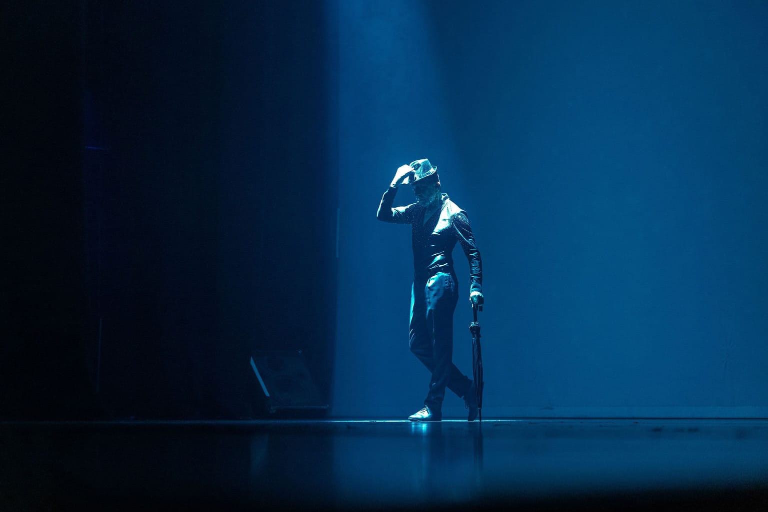 A performer on stage wearing a hat and holding an umbrella