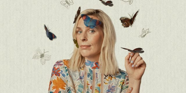 Comedian Sara Pascoe is pictured wearing a brightly coloured patterned top and surrounded by butterflies. A butterfly is sitting on her hand and 2 are on her head.