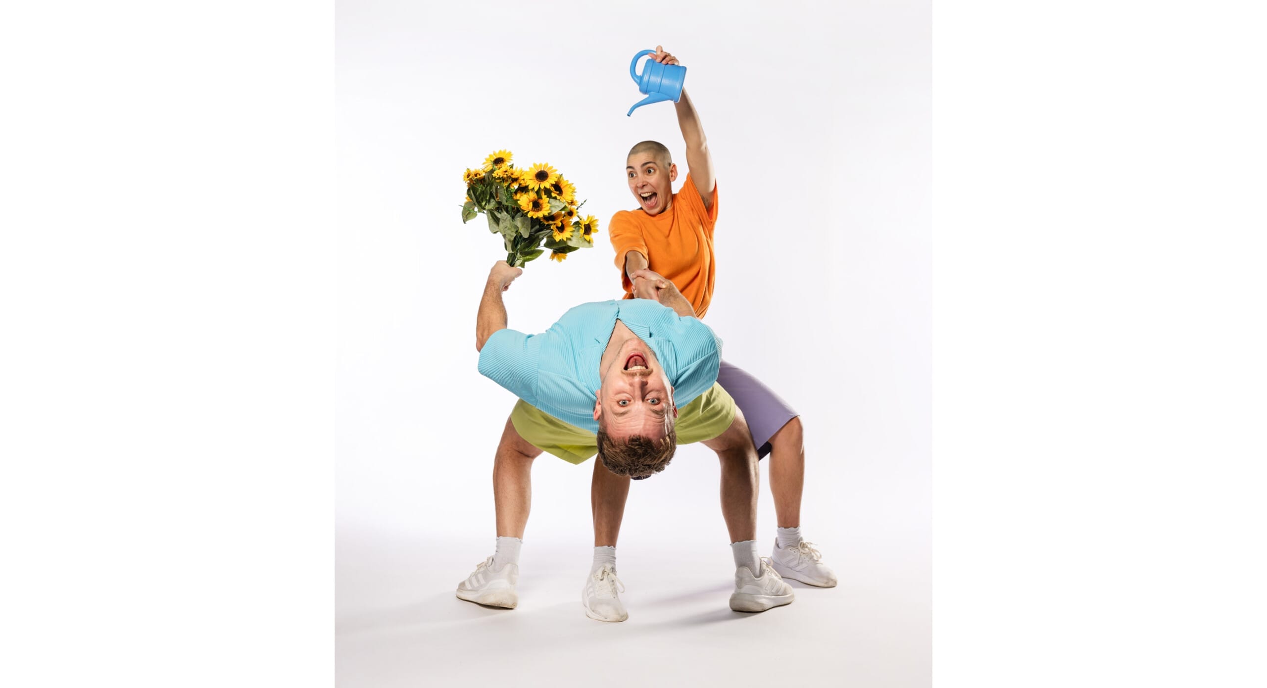A man holding a bouquets of flowers is bending backwards, whilst a woman with shaved head pretends to water the flowers with a watering can.