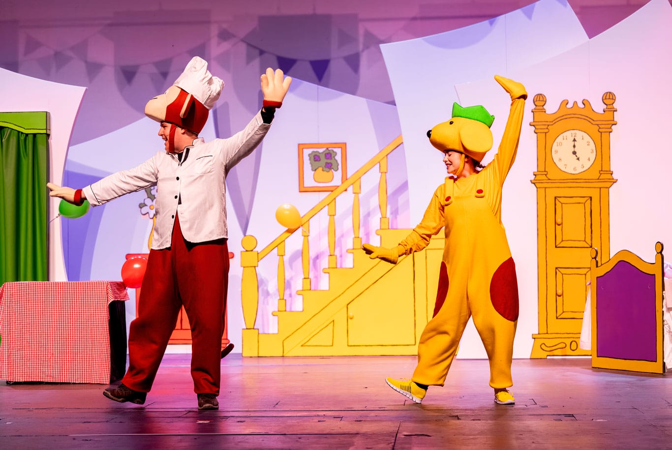 Two performers on stage in Spot's Birthday Party, one is dressed as Spot the dog and the other is dressed as a monkey. They are doing identical dance moves with one arm in the air.