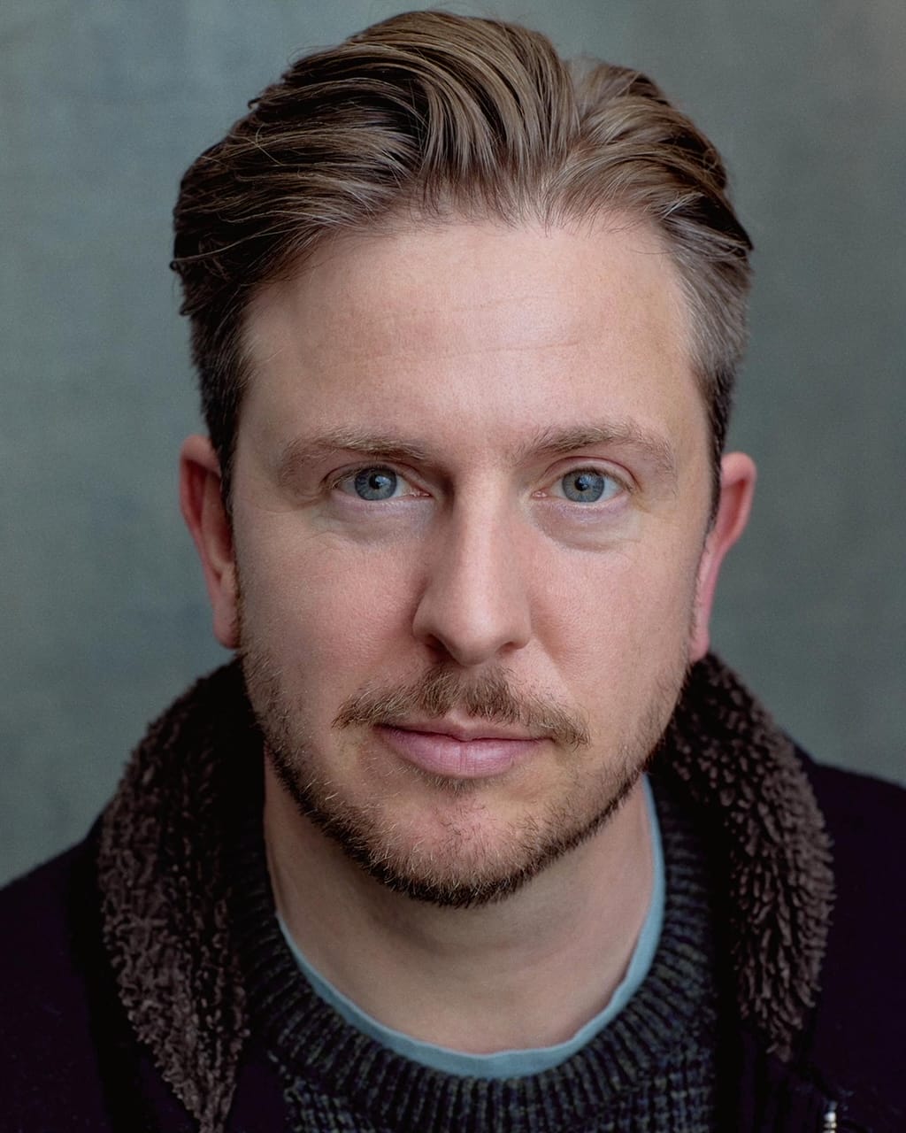 Head shot of Tom Richardson. A white man with blond hair and blue eyes wearing a black hoody.