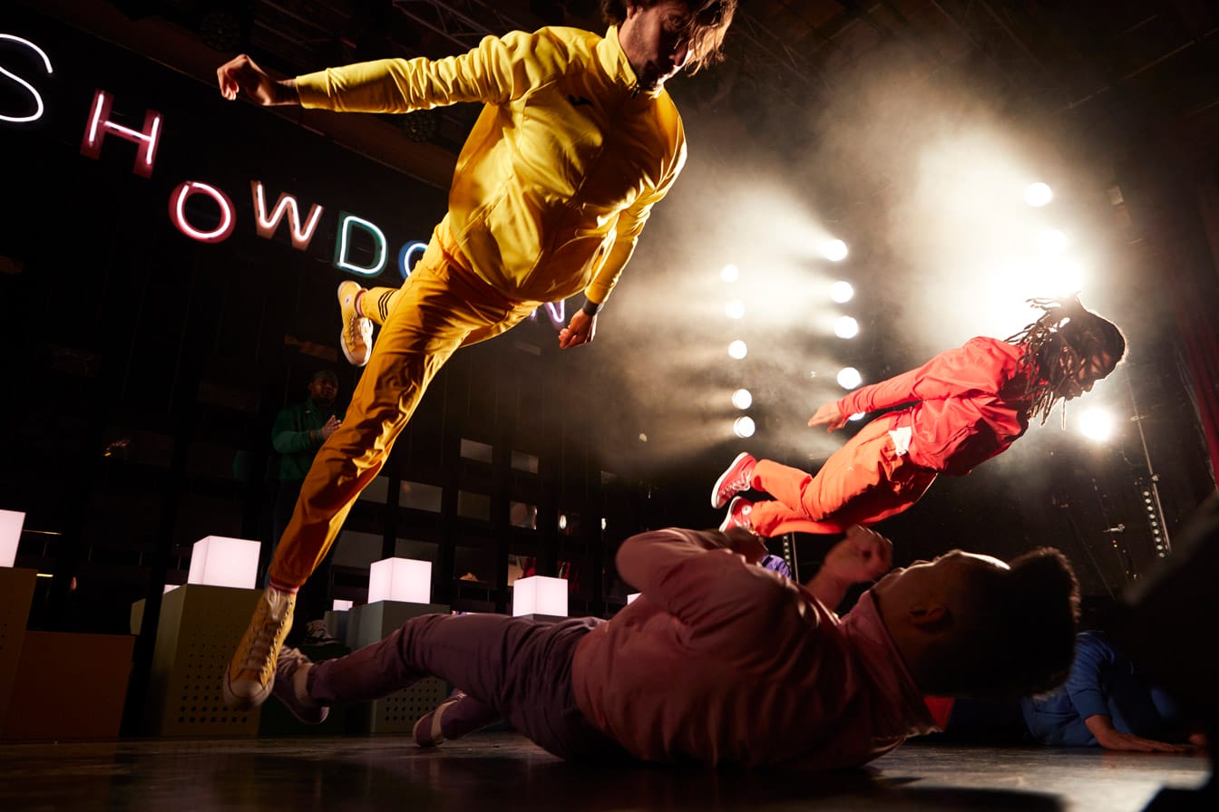 Two performers in Showdown launch themselves forwards wearing brightly coloured tracksuits, they are pictured from below