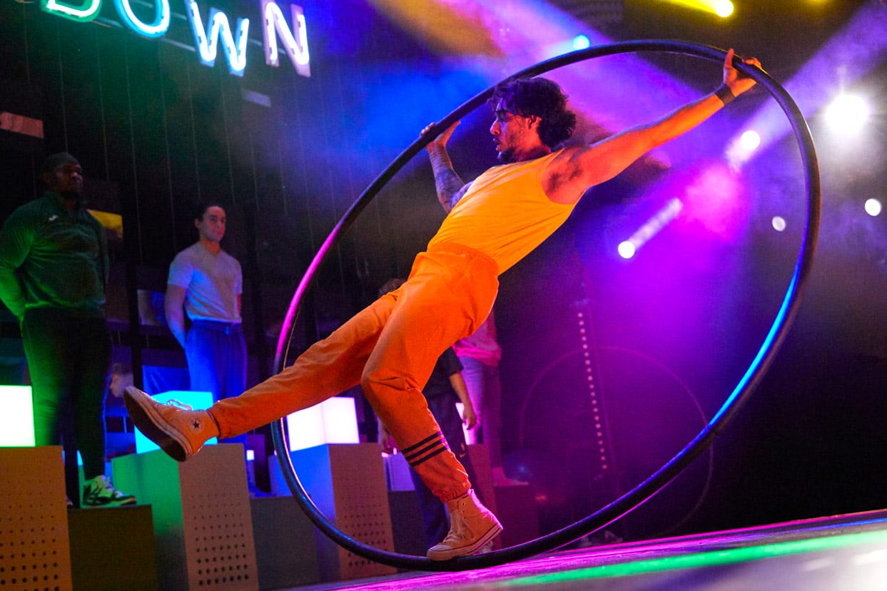 A performer on a cyr wheel in Showdown. He is pictured from below and is in a dynamic pose.
