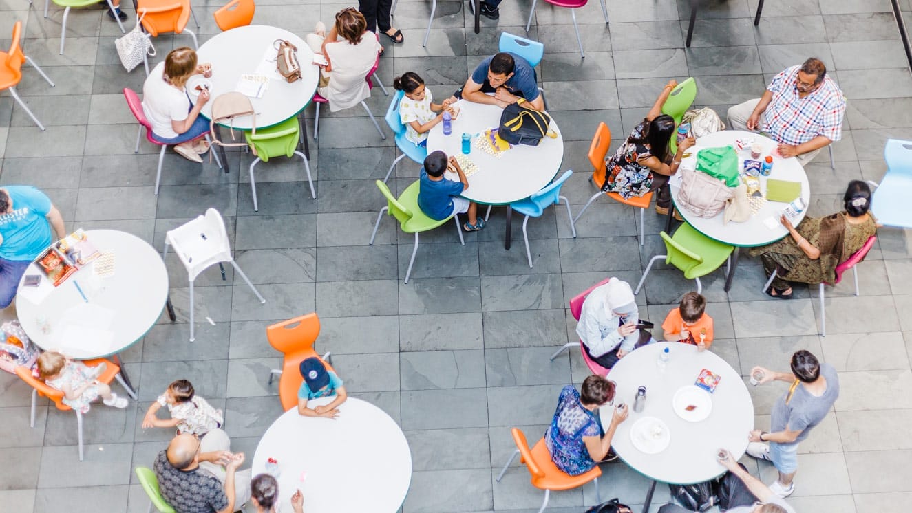 An image of artsdepot's cafe taken from above. People of all ages are sitting at round tables.