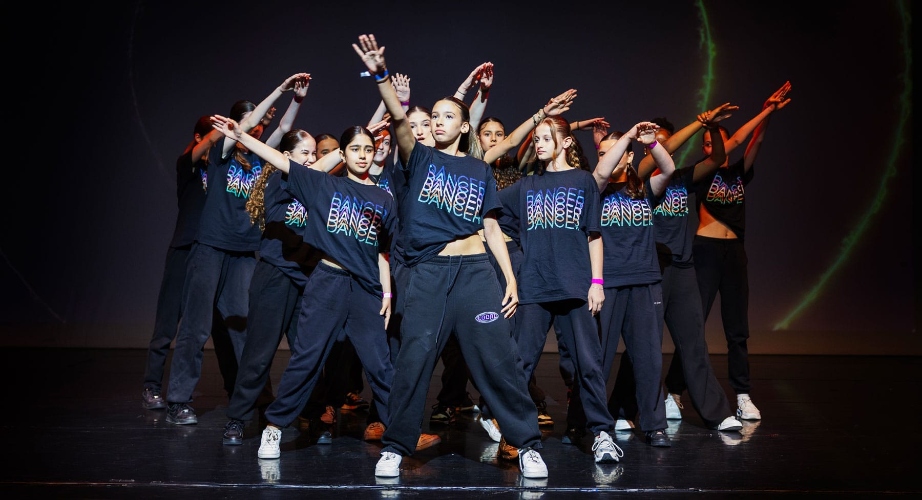 A group of diverse young dancers holding one hand high up on stage.
