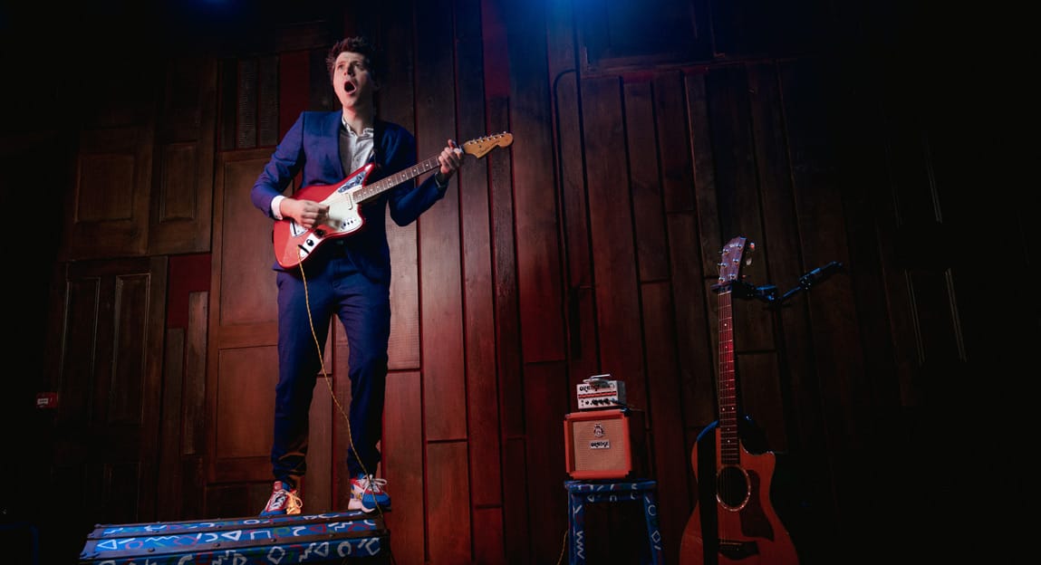 David Gibbs passionately performs on stage with an electric guitar, mouth open in song.