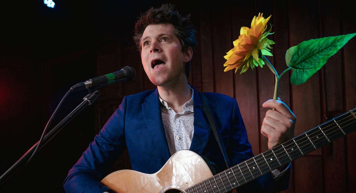 David Gibb performs with guitar and a sunflower in hand.