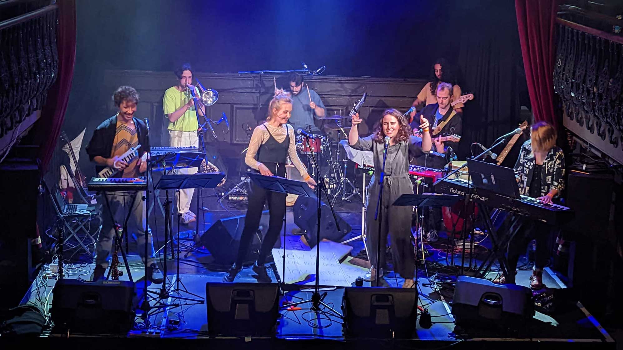 The Coveryard ensemble are captured performing on stage.