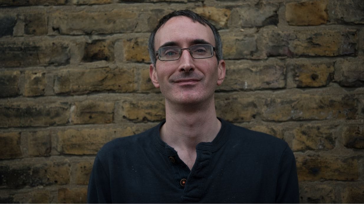 A man poses for a photo against a brick wall.