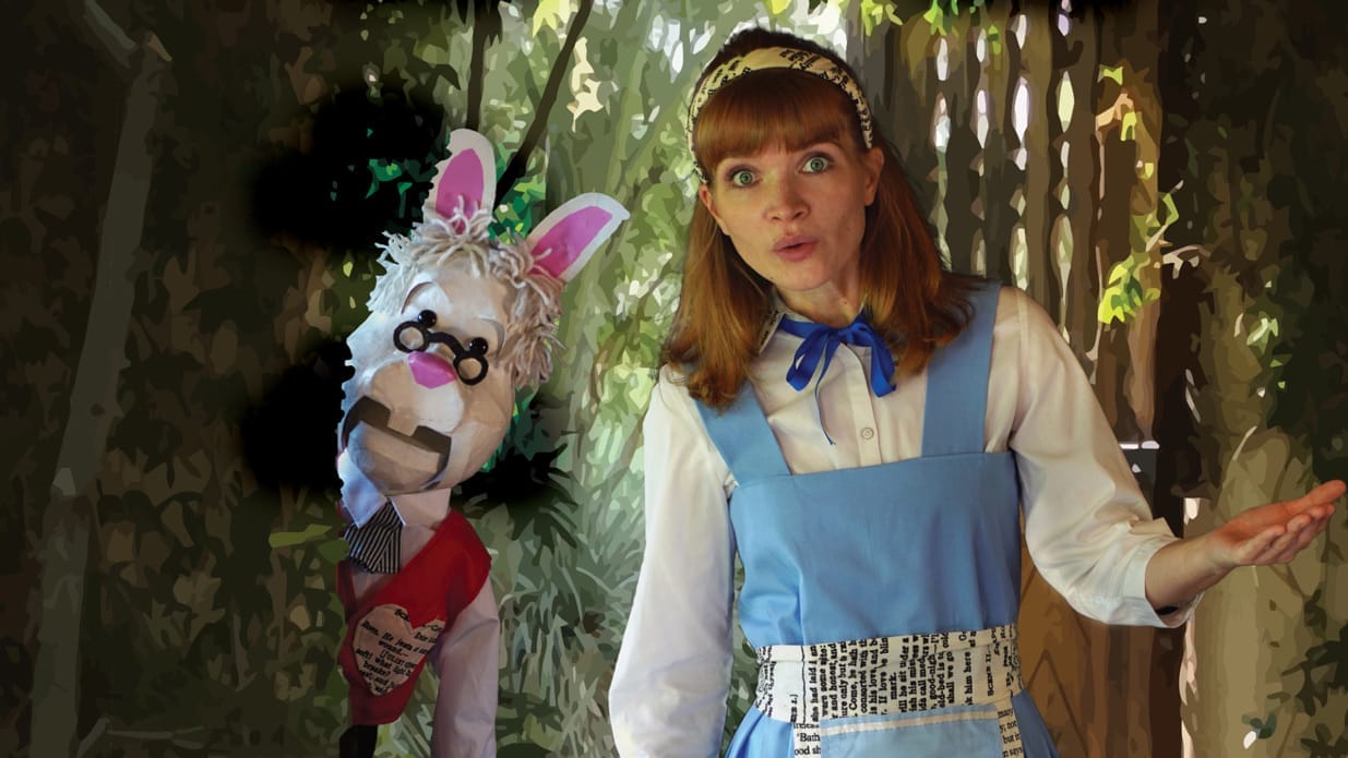 A performer wearing the traditional blue dress and white shirt of Alice in Wonderland is pictured in a garden. Next to her, a puppet of a white rabbit wearing glasses looks out from behind a tree.