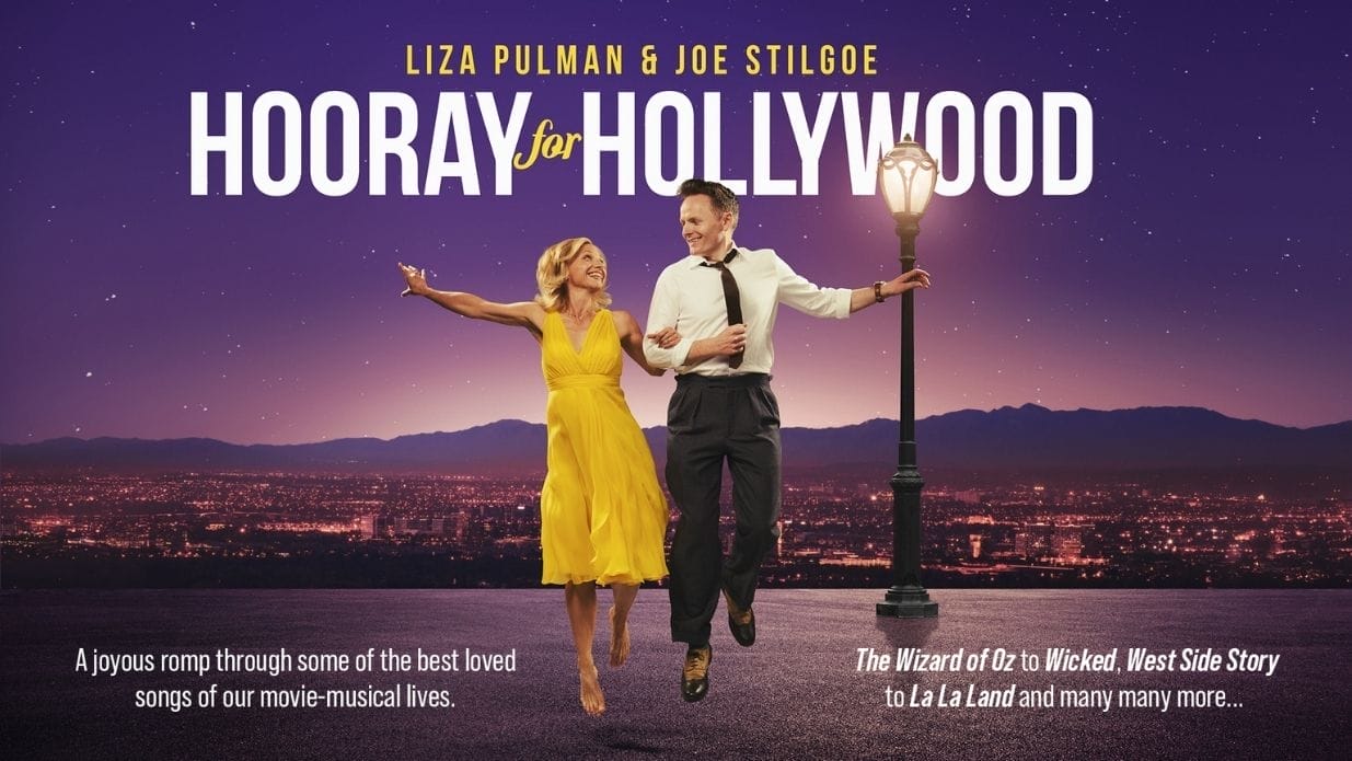 Liza Pulman, wearing a bright yellow dress and Joe Stilgoe, wearing a black tie, white shirt and black trousers are jumping arm in arm. Behind them is a street lamp and the Hollywood hills. The image is reminiscent of the film La La Land. White text on the image reads Hooray for Hollywood.