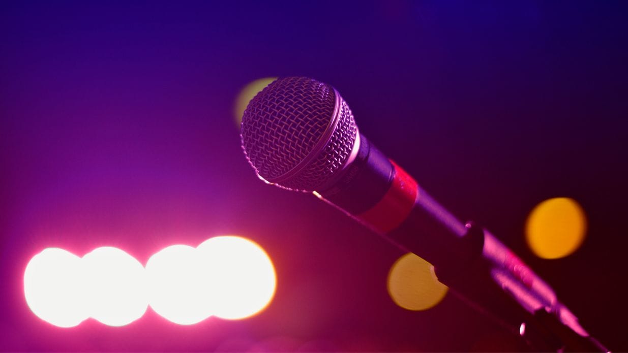 Image of a mic set against a brightly lit background of pink and purple lights.