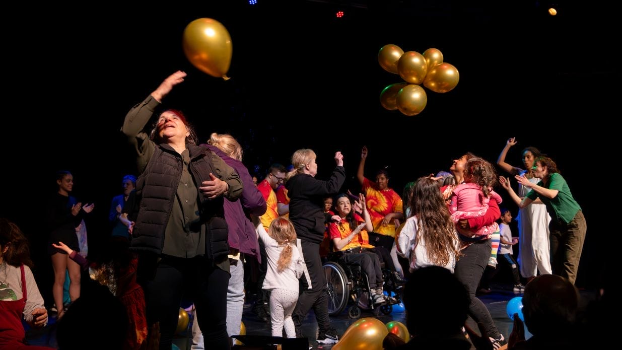 A crowd of people gathered on a stage playing with balloons.