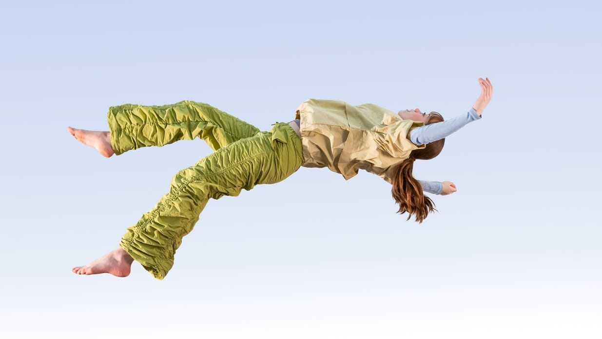 A dancer wearing a green and gold costume falls backwards as if suspended in the air