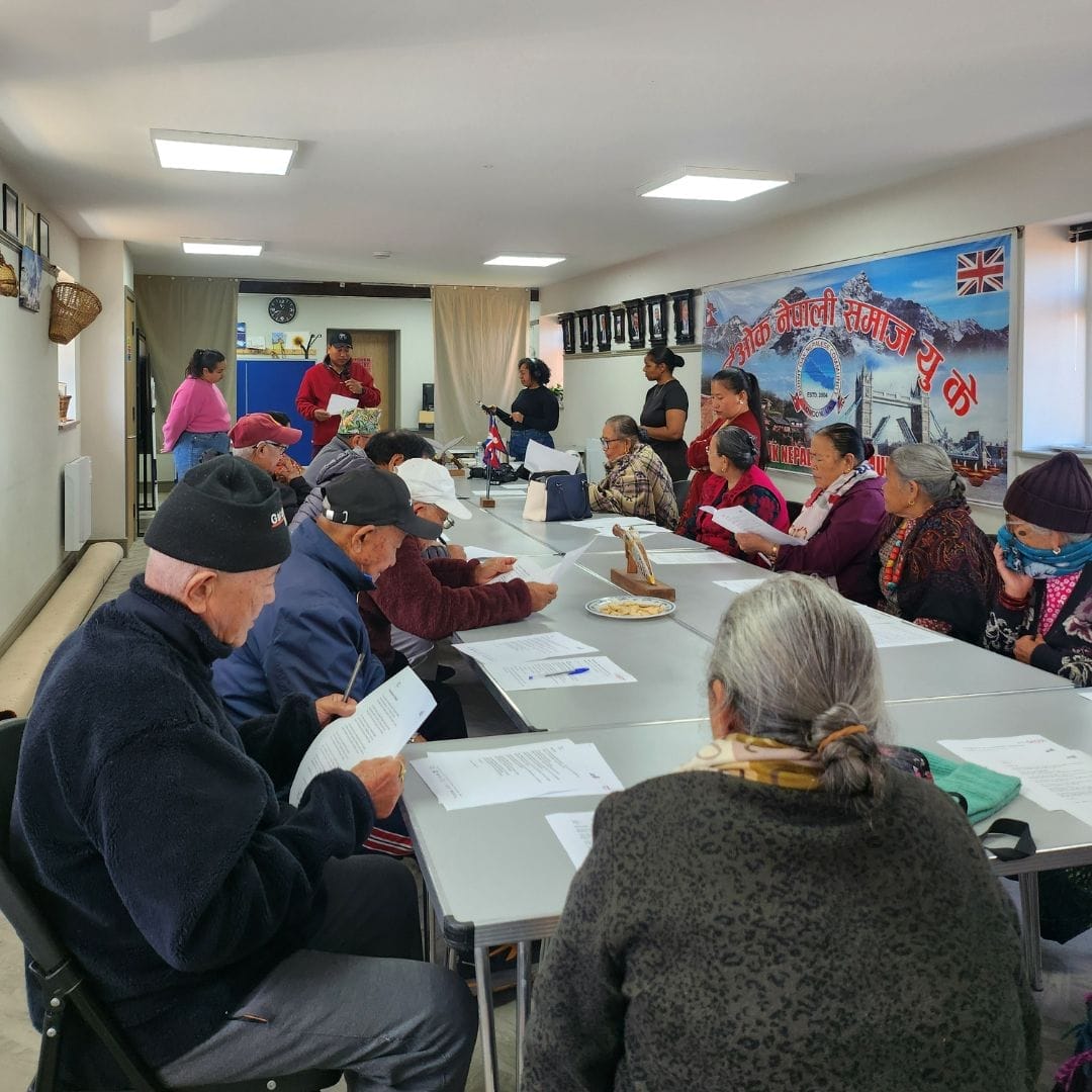 A group of elderly people sit around a large desk.
